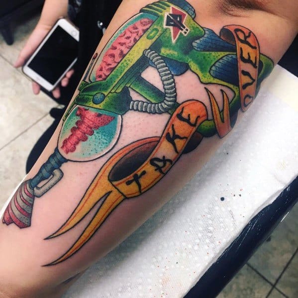 Colorful ray gun tattoo with a sci-fi design, featuring bold shading and a ribbon wrapping around with the words "Take Over" written on it.