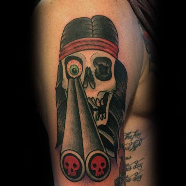 Bold neo-traditional shotgun tattoo featuring a skull with a red headband, staring down dual barrels decorated with skull motifs.