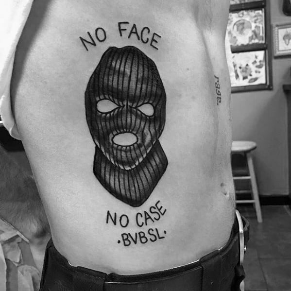 Tattoo of a ski mask on a man's side with the words NO FACE above and NO CASE BVB5L below in bold black ink.