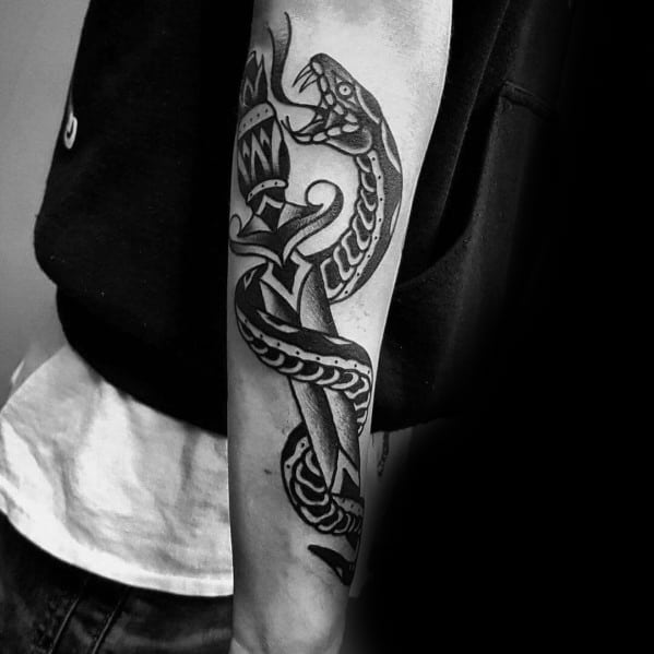 Black ink snake and dagger tattoo on forearm, featuring bold lines and intricate details in a classic traditional style.