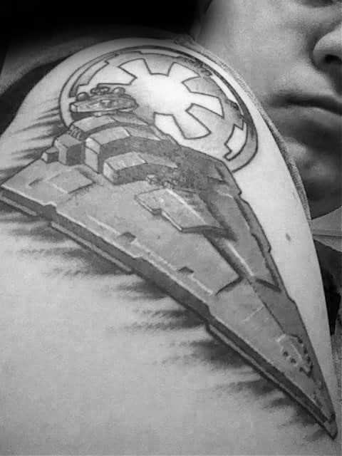 Star Destroyer tattoo on shoulder with Galactic Empire emblem in the background, detailed in black and gray ink.