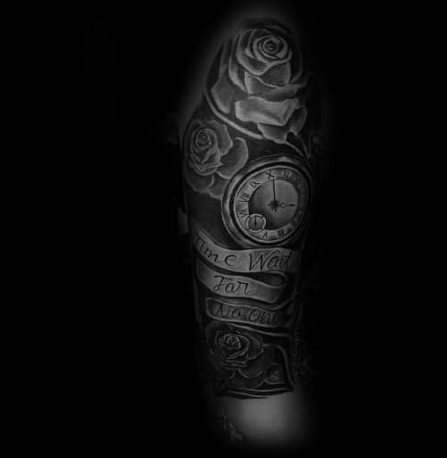 Black and grey tattoo with roses, a clock showing 3:15, and scroll text reading Time Waits for No Man on a man's upper arm.