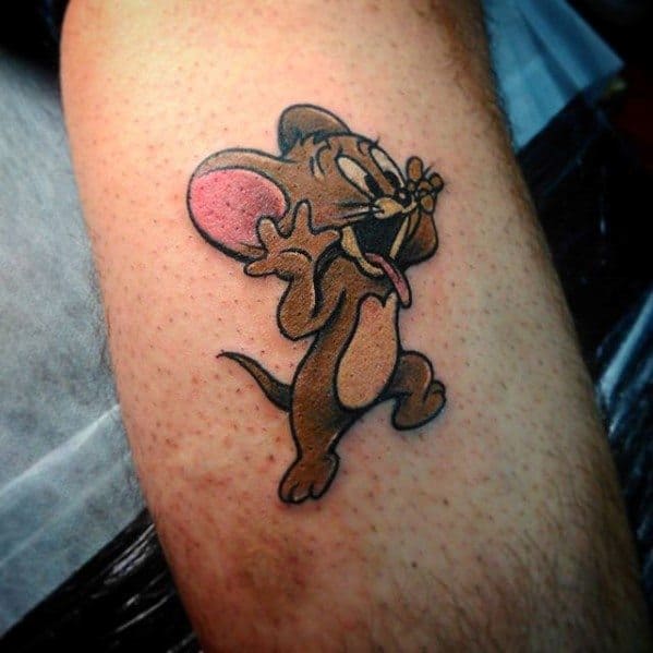 Tom and Jerry tattoo of Jerry with tongue out and hands up, inked on a man's arm in a playful cartoon style.