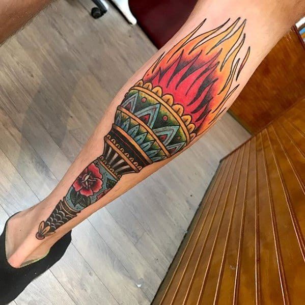 Bold torch tattoo on the calf featuring vibrant flames, tribal patterns, and a red flower near the base of the handle.
