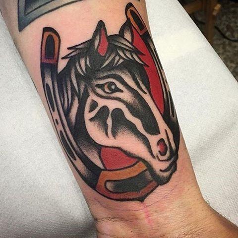 Traditional horse tattoo design for men featuring a black and white horse head with a horseshoe and bold red background.