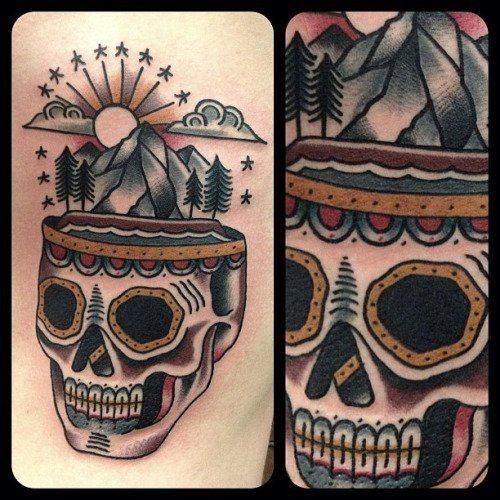 Traditional skull tattoo with mountains, trees, and sun rising from the top, blending nature and bold old-school design.