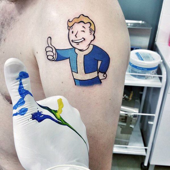 Vault Boy tattoo on upper arm featuring the iconic thumbs-up pose, freshly inked in a clean, vibrant style.