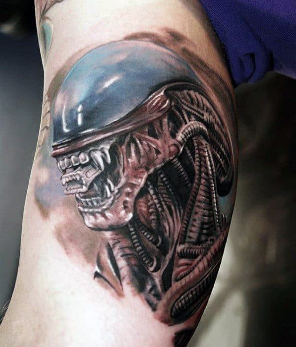 Realistic Xenomorph tattoo on upper arm with detailed biomechanical elements and a glossy, dome-shaped head.