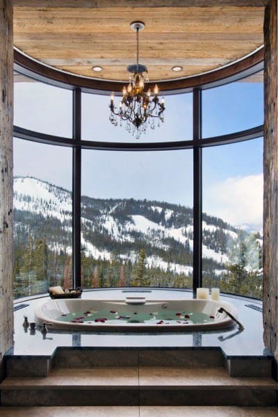 Rustic yet luxurious bathtub with mountain view and chandelier overhead