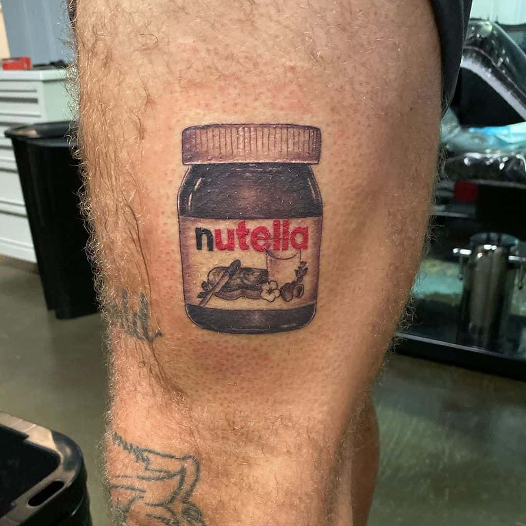 A realistic tattoo of a Nutella jar on the thigh, detailed with shading and branding, creating a bold food-themed design.