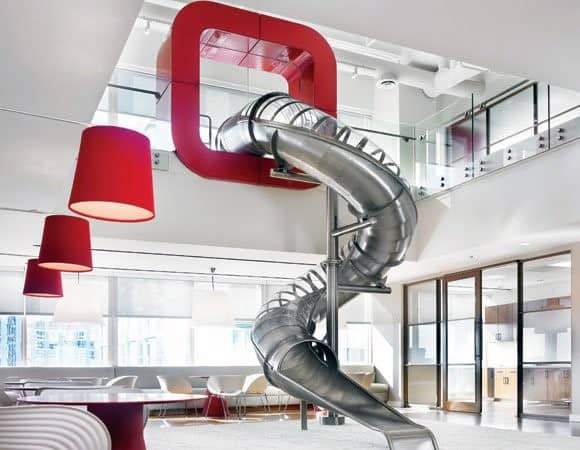 Modern office with a slide linking floors, featuring red accents and open workspaces