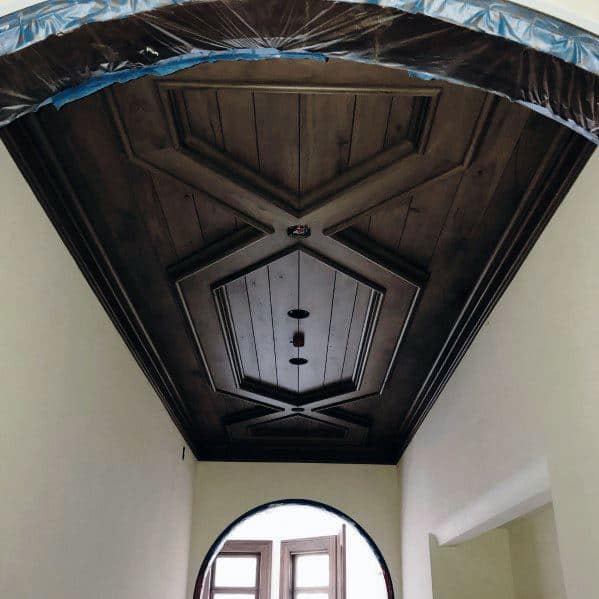 Ornate dark wood ceiling with geometric design in a narrow front foyer.