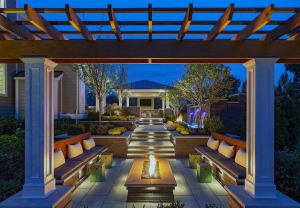 Modern patio with pergola, built-in seating, fire feature, and illuminated pathways at night.