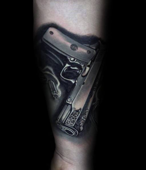 Realistic black and gray tattoo of a 1911 pistol on the forearm, featuring intricate engravings and detailed shading for a three-dimensional effect.