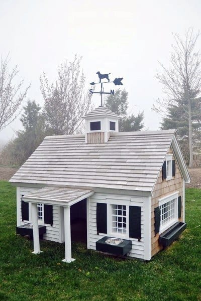 A miniature doghouse styled like a barn with a weather vane on the roof
