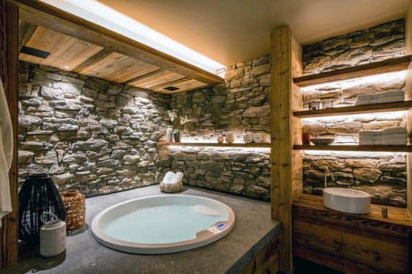 Rustic bathroom with stone walls, round tub, and wooden shelves