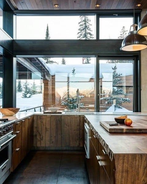 Rustic kitchen with wooden cabinets, large windows, mountain views, and industrial lighting.
