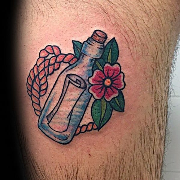 Tattoo of a message in a bottle with a note, flower, and rope on skin
