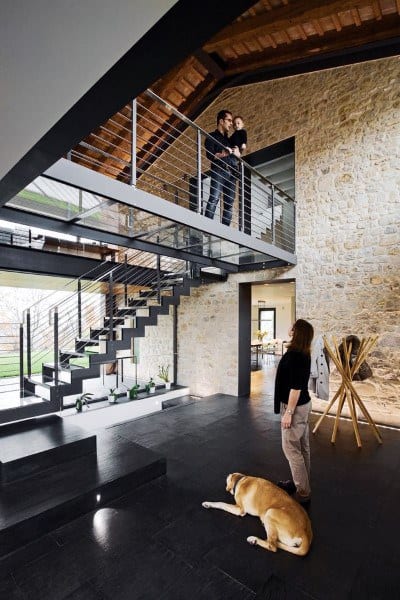 A modern home interior with a dog on the floor, people on the staircase and balcony, and stone and wood accents