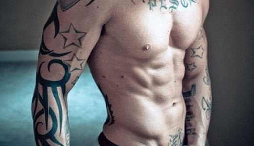 Shirtless person with various tattoos on arms and upper body