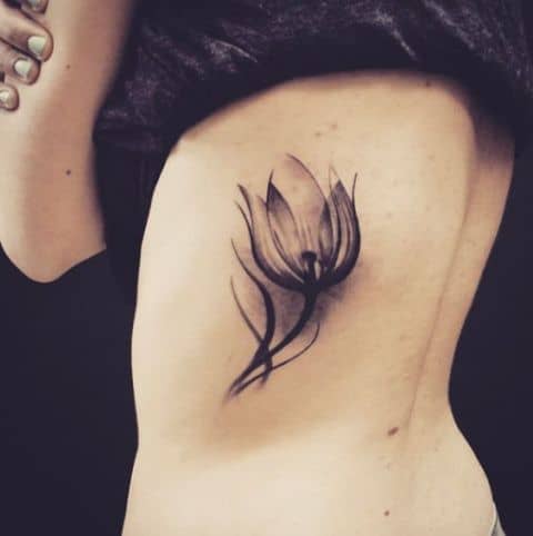 A bold black tulip tattoo on the side of the torso, featuring a large, dramatic flower with flowing lines and soft shading.