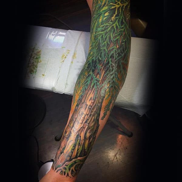 Vibrant full-sleeve tattoo of a massive tree with intertwining roots and lush green foliage, creating a nature-inspired, immersive design.