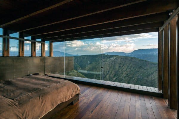 Bedroom with glass walls overlooking scenic mountains and a wooden interior.