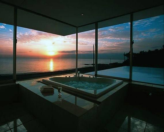 A luxurious bathtub with a sunset ocean view through large windows