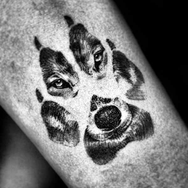 Black and grey tattoo of a wolf’s face artistically shaped into the form of a paw print, located on the forearm