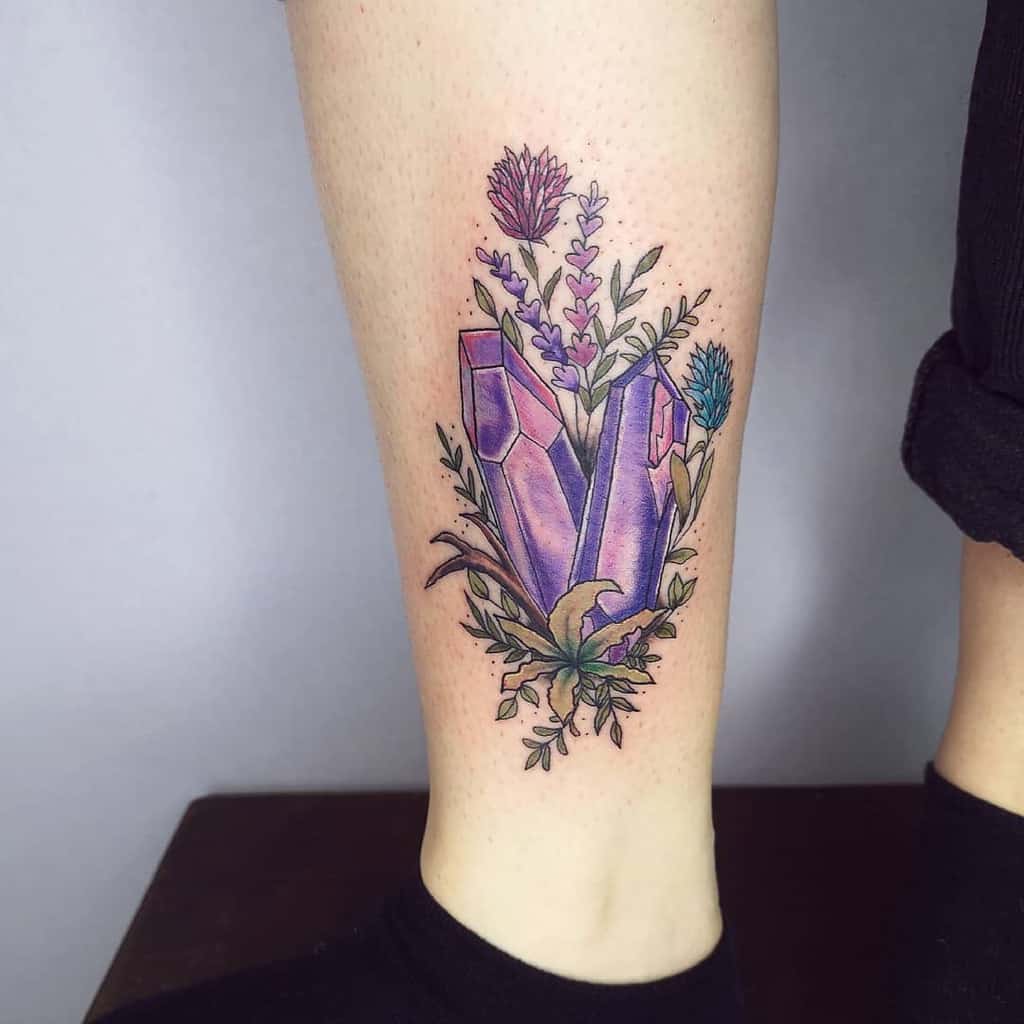 A vibrant tattoo featuring a geometric crystal surrounded by lavender and greenery, with soft colors and intricate detailing on the lower leg.