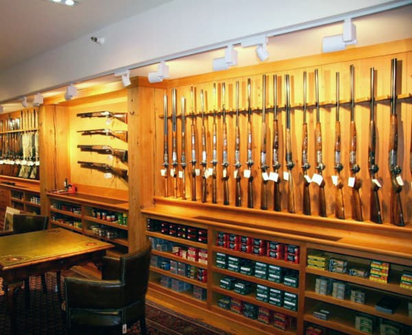 Gun room with wooden racks displaying rifles and shelves stocked with ammunition boxes.