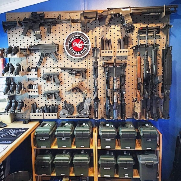 Gun room with a pegboard displaying firearms, accessories, and ammo boxes on shelves below.