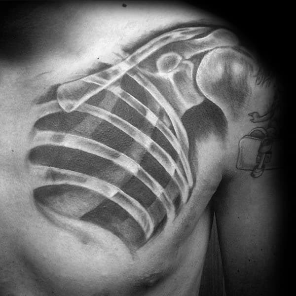Black and grey chest tattoo of an exposed ribcage and shoulder bones, designed to resemble an anatomical X-ray view.