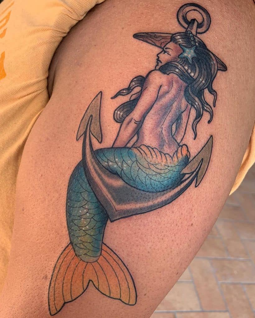 Bold tattoo of a siren entwined with an anchor, featuring shimmering blue and orange scales, flowing hair, and a nautical theme