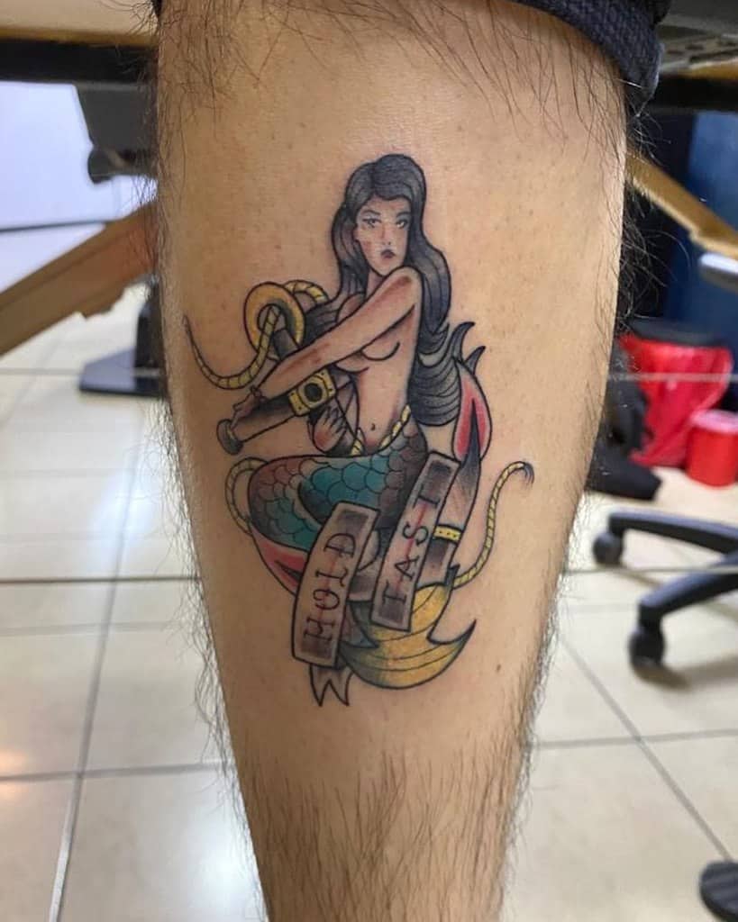 Tattoo of a sailor siren on a leg, holding rope and anchor with "Sail Fast" banner