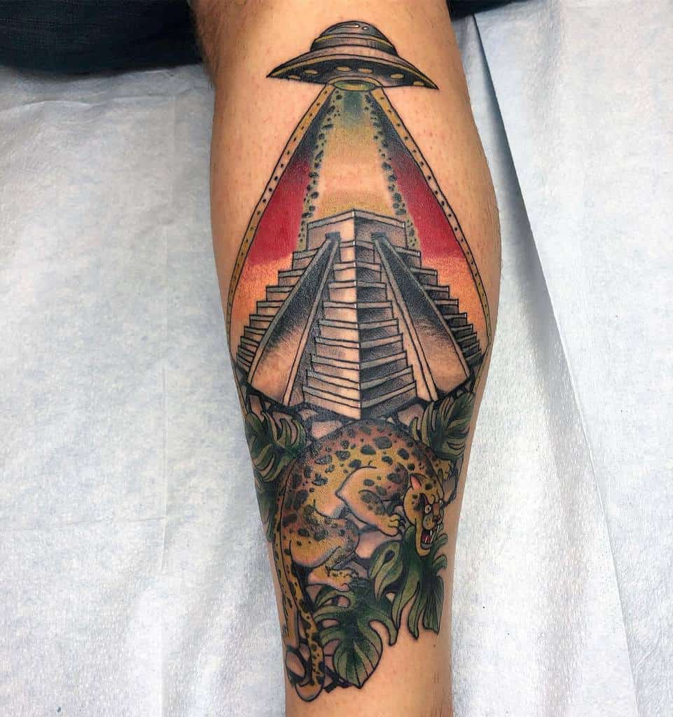 A vibrant tattoo featuring a UFO beaming down over an ancient pyramid, with a jaguar below surrounded by tropical leaves, blending mystical and natural elements.