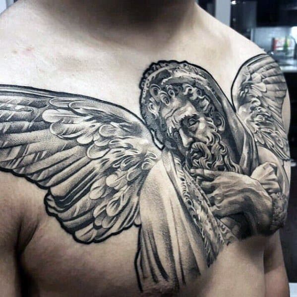 A detailed black and grey tattoo of a bearded figure with wings, covering the chest area of a man.