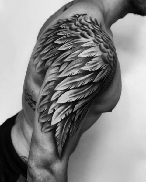 Black and grey shoulder and upper arm tattoo featuring a detailed angel wing with realistic feather shading for a bold and dynamic design.