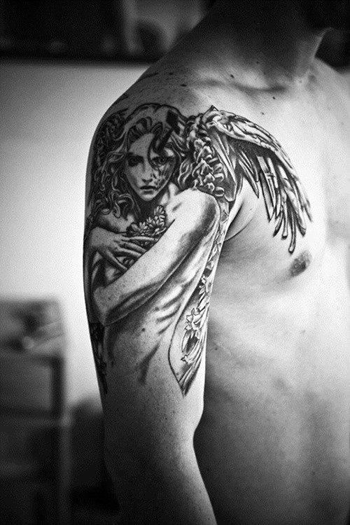 Black and white tattoo of an angel embracing flowers on a man's upper arm and shoulder