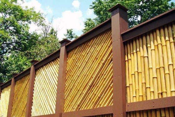 Decorative bamboo fence with wooden frame in a backyard surrounded by trees.