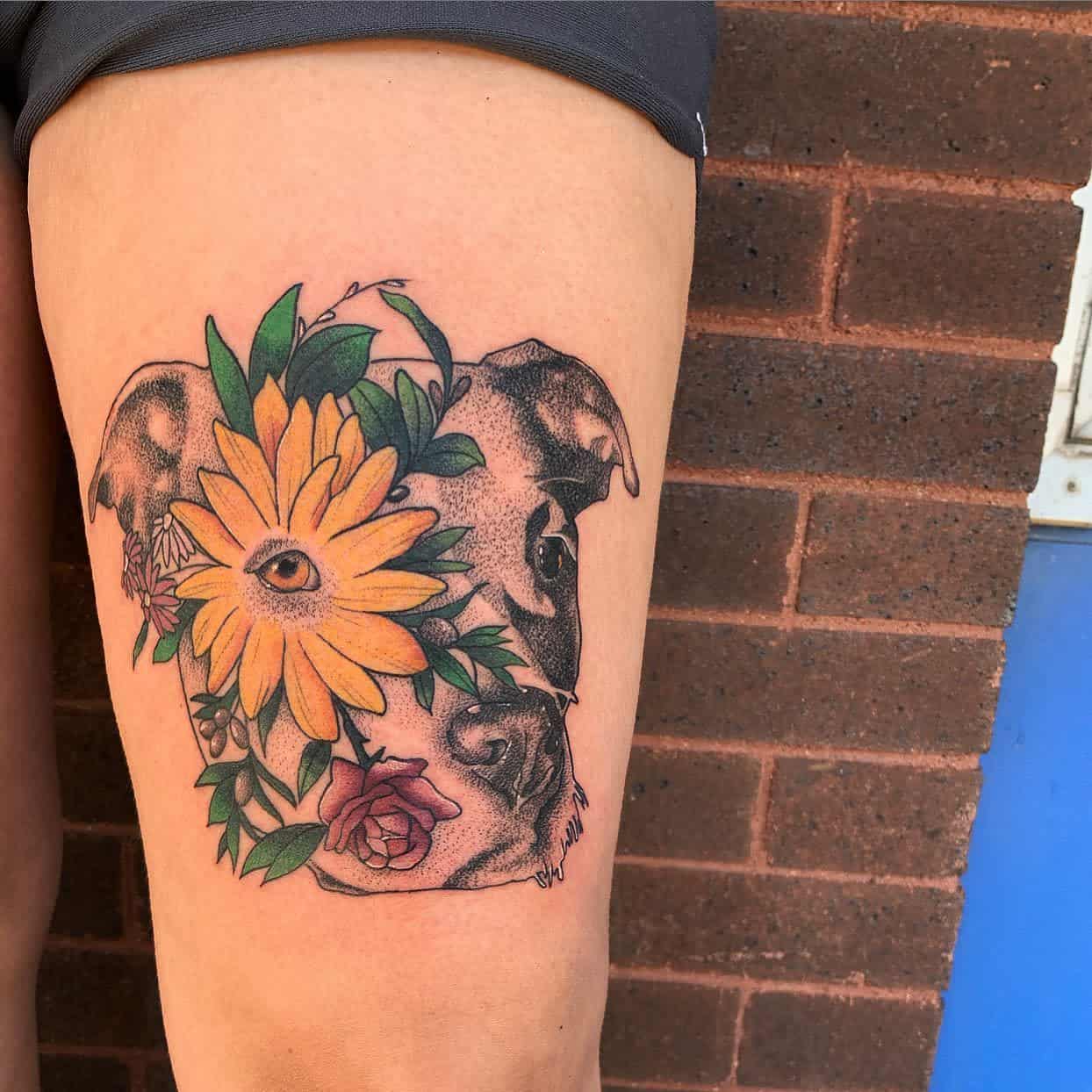 Tattoo featuring a dog's face intertwined with a large sunflower, other flowers and green leaves