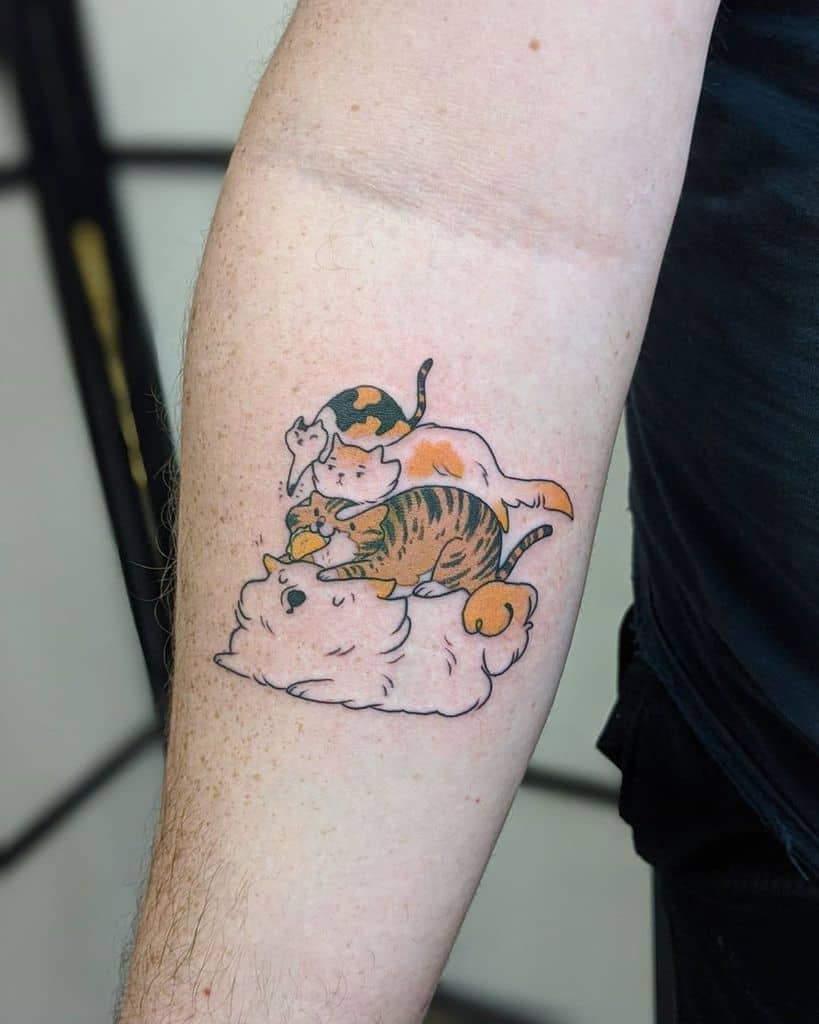 Whimsical tattoo featuring three playful cats, including a calico and a tabby, resting and interacting on top of a fluffy white cat
