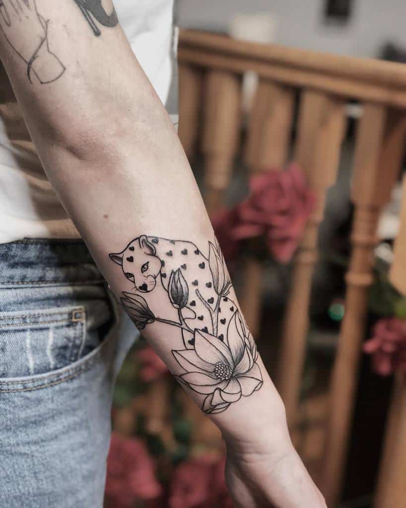 A delicate black and grey tattoo of a jaguar amidst floral elements, featuring a lotus flower and soft shading on the forearm.