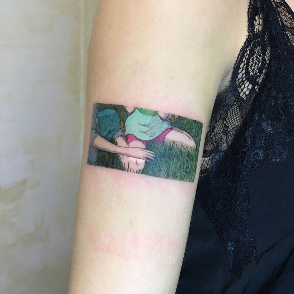Minimalist color tattoo of a memorable Spirited Away scene, showing Chihiro and Haku holding hands in the grass, framed like a film still