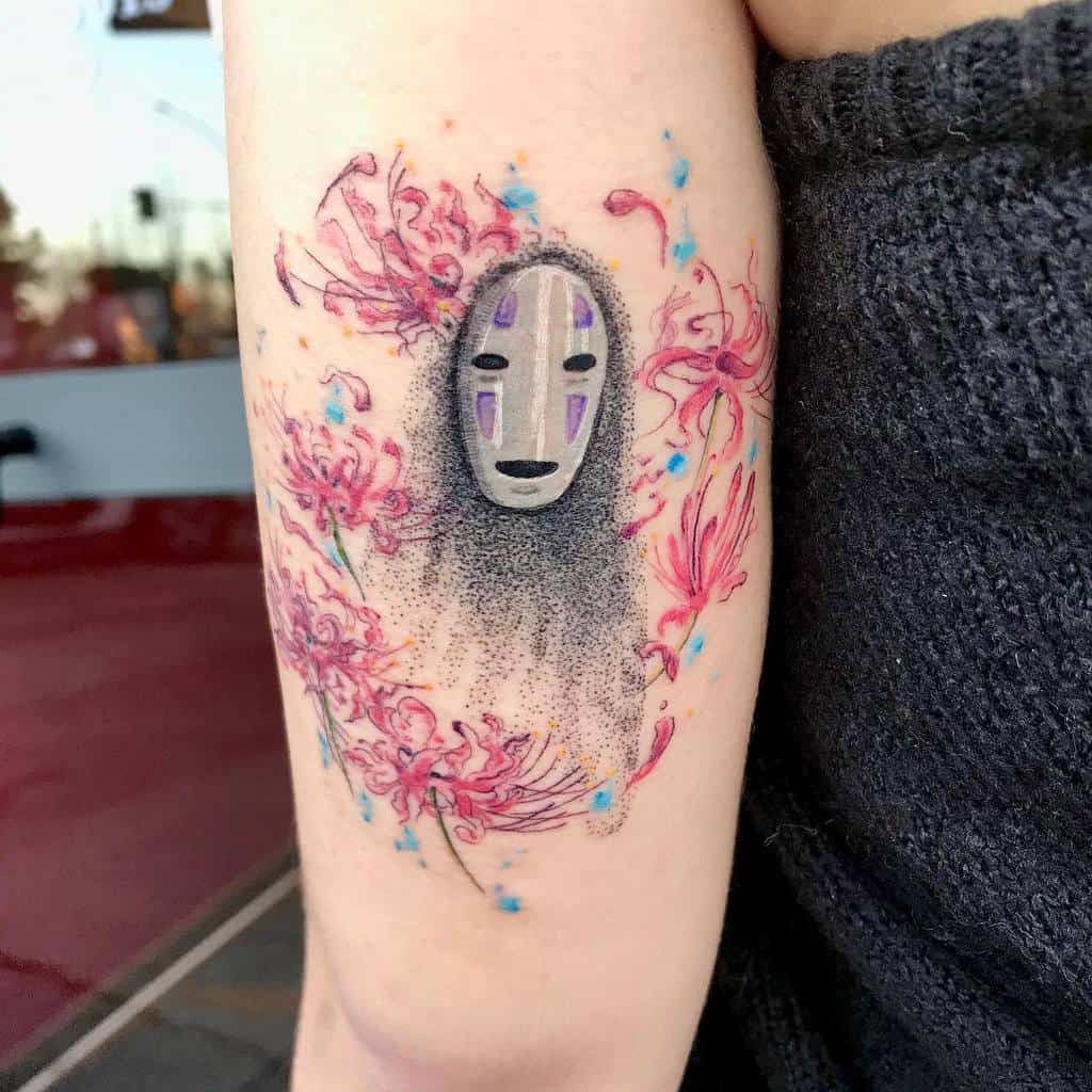 Delicate Spirited Away tattoo of No-Face, surrounded by soft pink spider lilies and watercolor splashes, blending fine dotwork and color