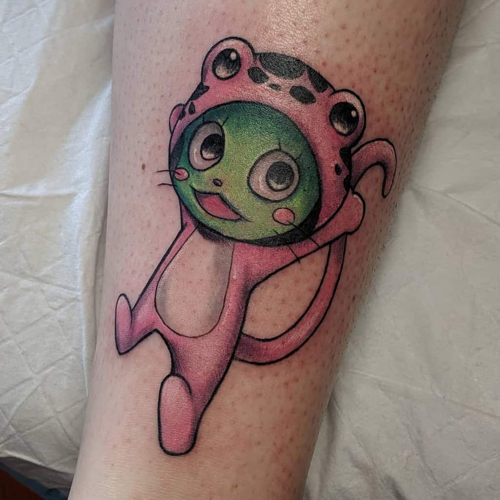 Colorful tattoo of Frosch from Fairy Tail, featuring vibrant green and pink tones with a cheerful expression and playful pose on the leg.