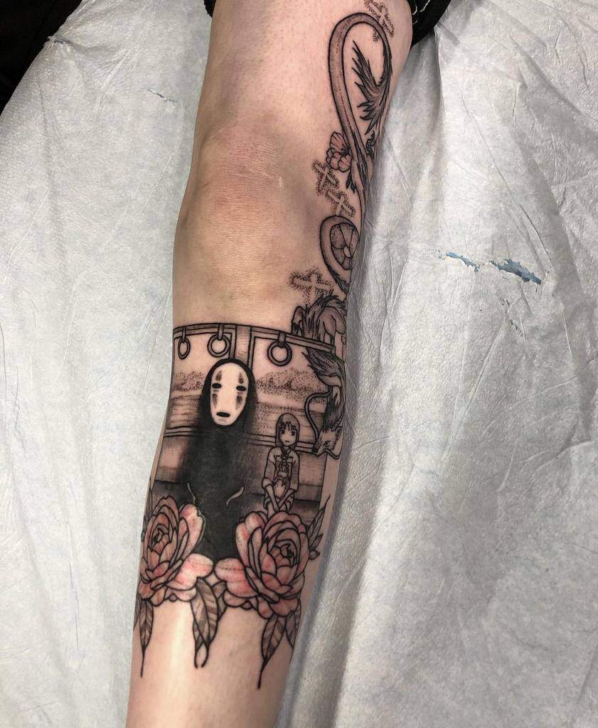 Detailed black and grey Spirited Away tattoo featuring No-Face and Chihiro on the train, framed by roses, with Haku in dragon form above