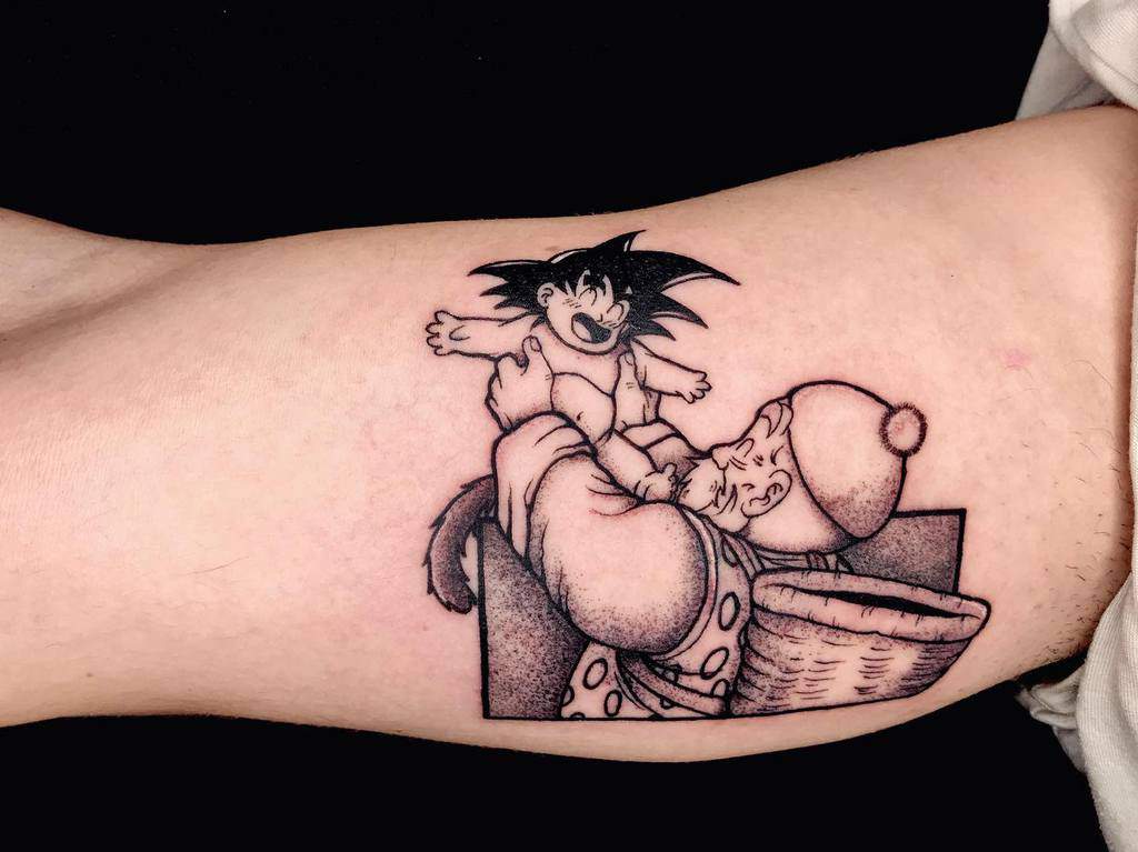 A tattoo of Goku as a baby being held by Grandpa Gohan from Dragon Ball, in black and white ink.