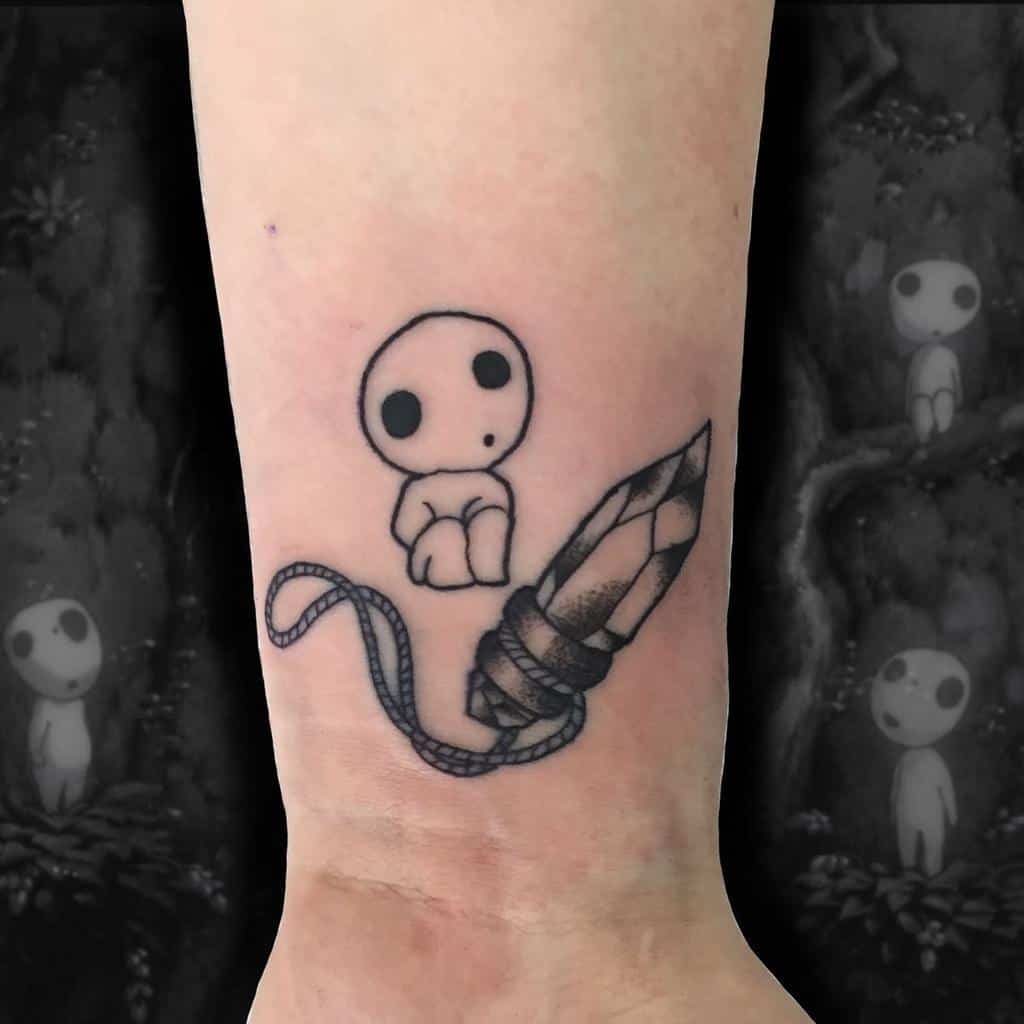 Small black ink tattoo of a kodama spirit sitting beside a crystal with a rope tied around it, inspired by Princess Mononoke.
