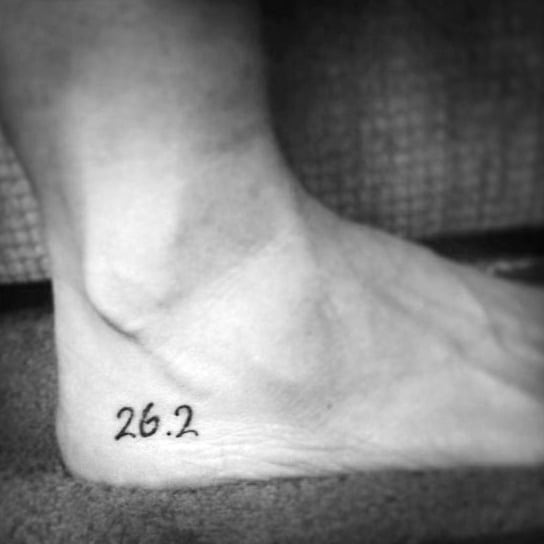 Simple and elegant 26.2 tattoo on the ankle, symbolizing a marathon runner’s dedication and achievement.